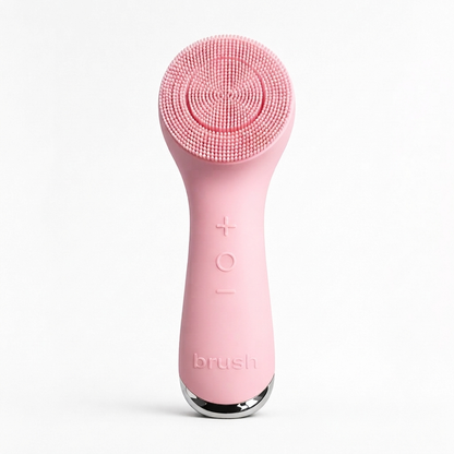 A pink handheld electric facial cleansing brush with a textured silicone brush head, featuring a silver metallic base and the brand name 'brush' embossed on the handle, set against a plain white background.